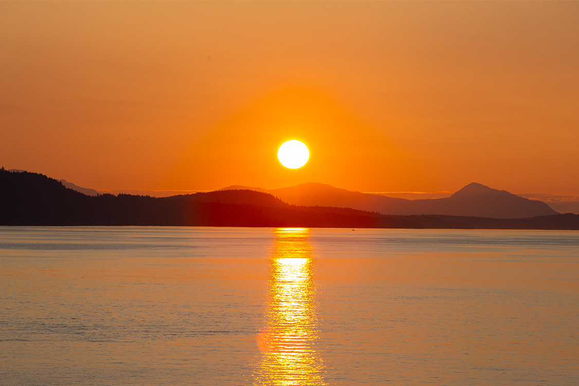 Sunset over calm water and distant mountain silhouettes